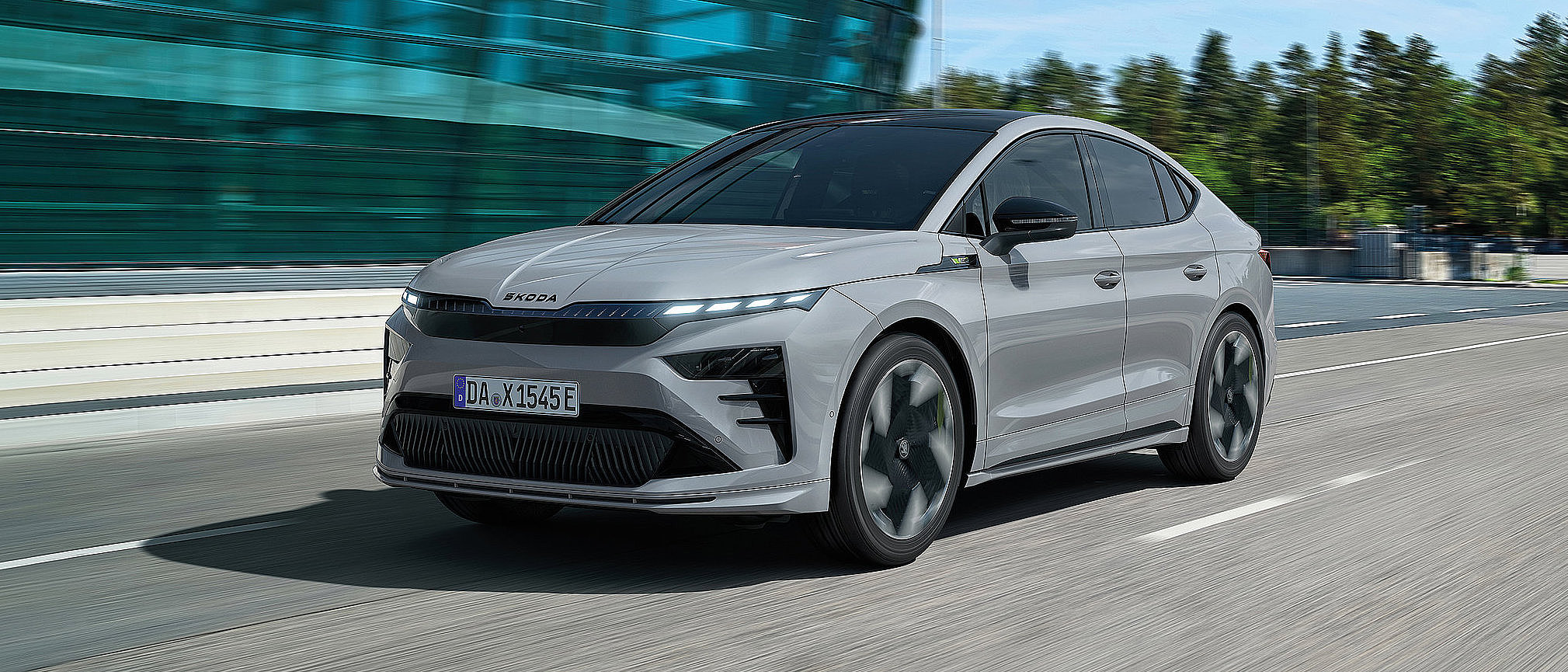 Weißes Škoda Enyaq Coupé als vollelektrisches Familienauto bei der Fahrt durch die Stadt, aufgenommen aus schräger Frontansicht.