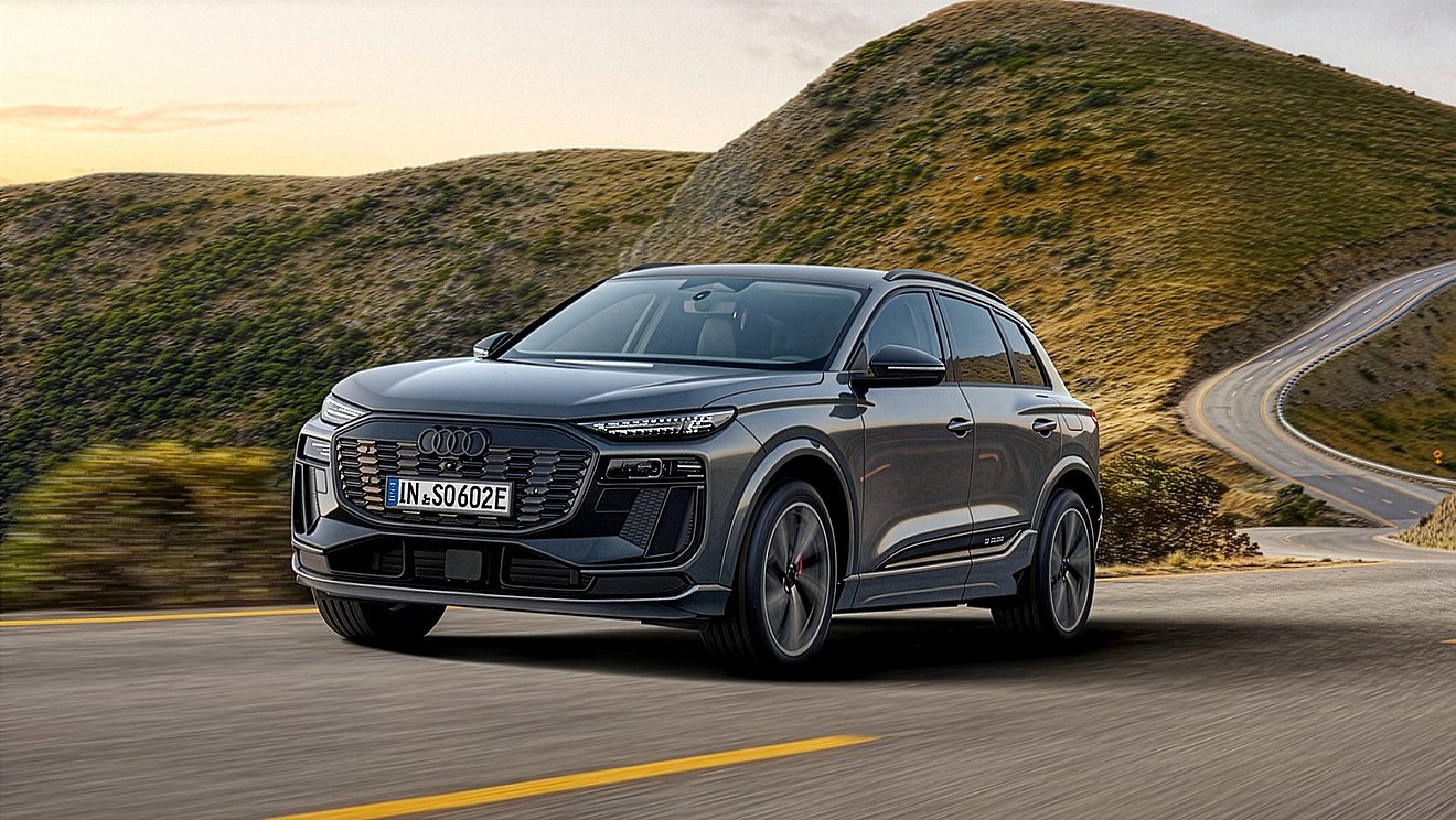 Grauer Audi Q6 e-tron als vollelektrisches SUV auf kurvenreicher Bergstraße – dynamische Front- und Seitenansicht während der Fahrt.