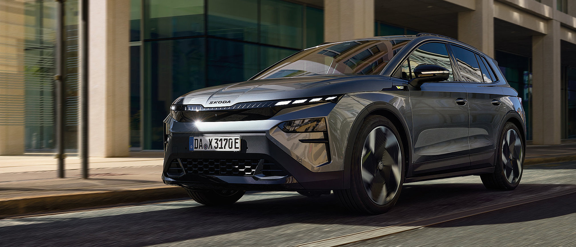 Grauer Škoda Elroq Elektro-SUV bei der Fahrt durch die Stadt, ideal für Kurzstrecken und den täglichen Stadtverkehr.