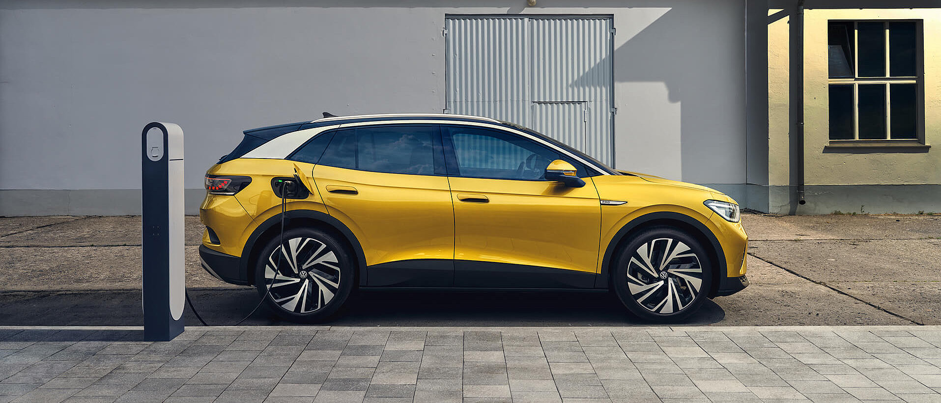 Gelbes Volkswagen Elektroauto wird an einer öffentlichen Ladesäule geladen.