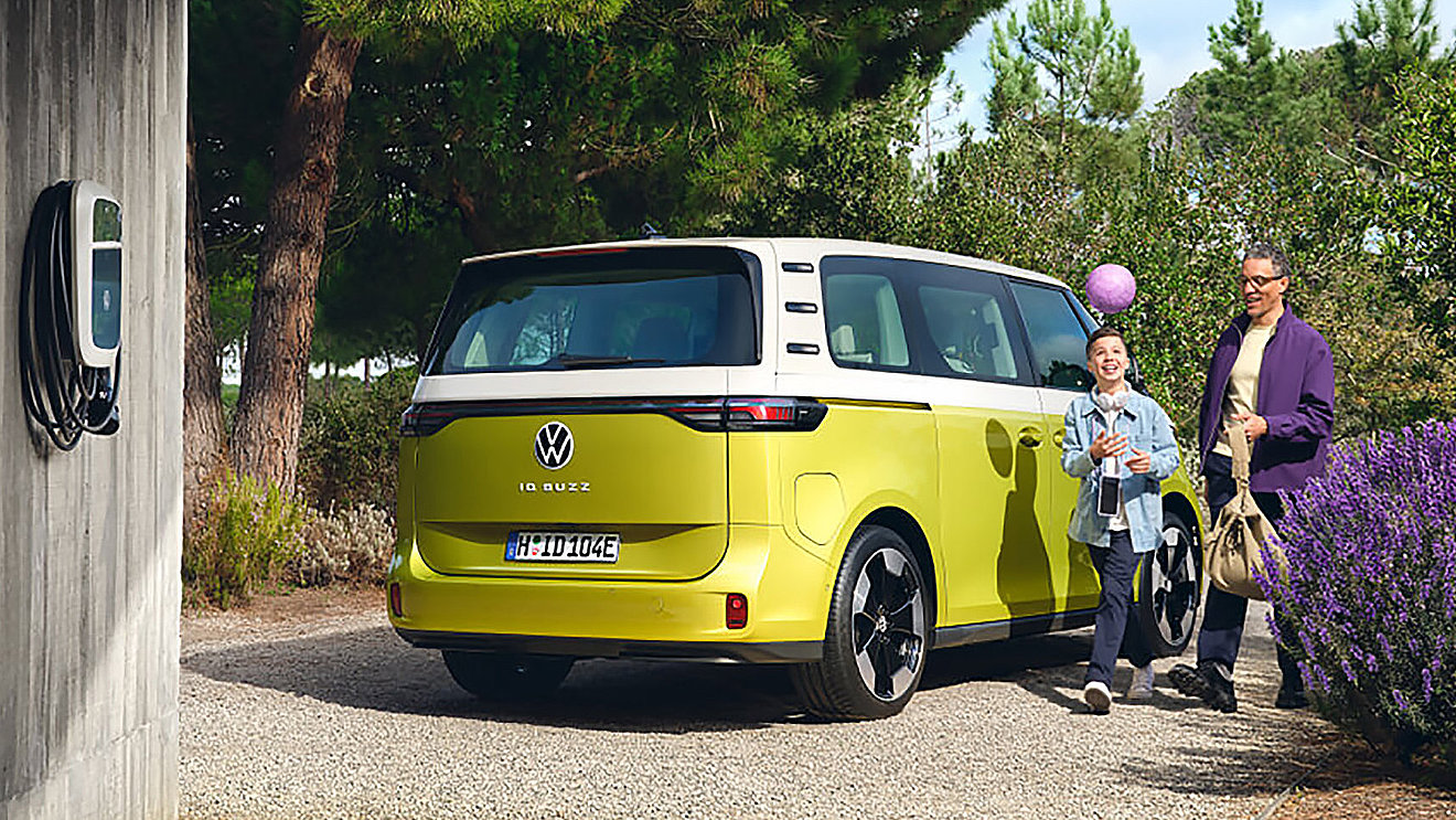 Gelb-weißer VW ID. Buzz Elektro-Van mit Vater und Kind neben einer Wallbox – geräumiges Familien-Elektroauto mit flexibler Nutzung und viel Platz für den Familienalltag.
