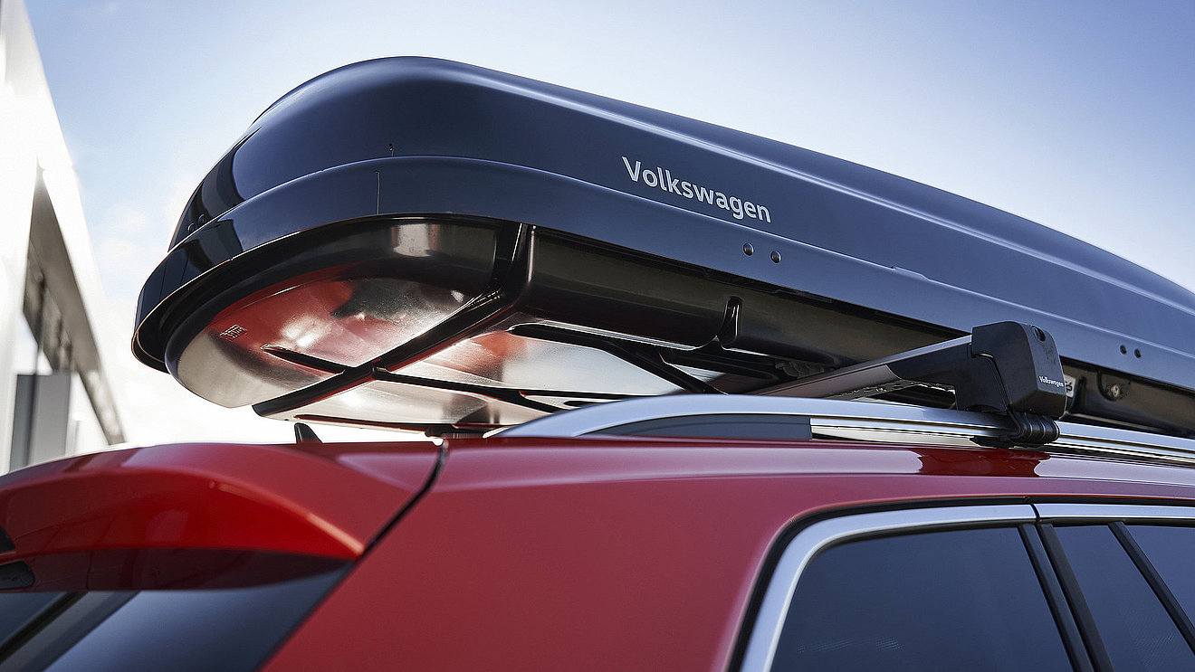 Volkswagen Dachbox auf dem Dachträger eines roten Fahrzeugs als praktisches Mietzubehör.