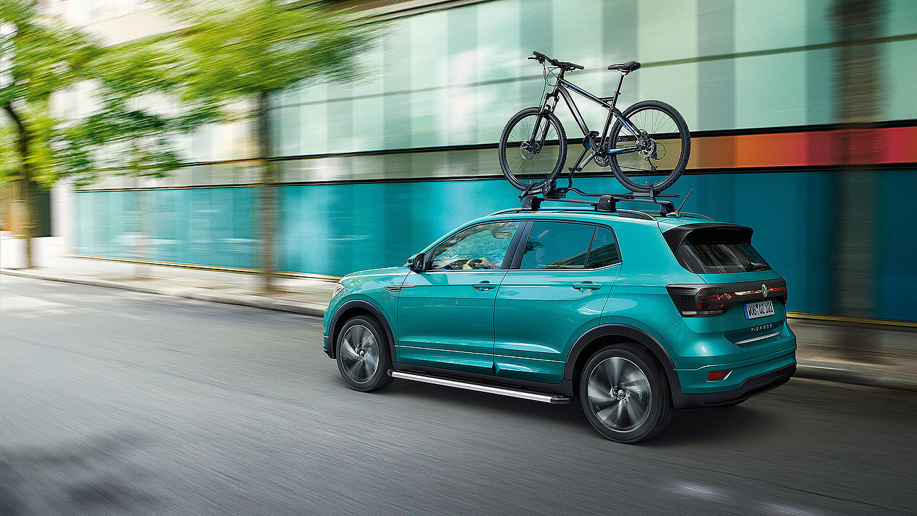 Volkswagen T-Cross mit Fahrradträger auf dem Dach unterwegs in der Stadt.