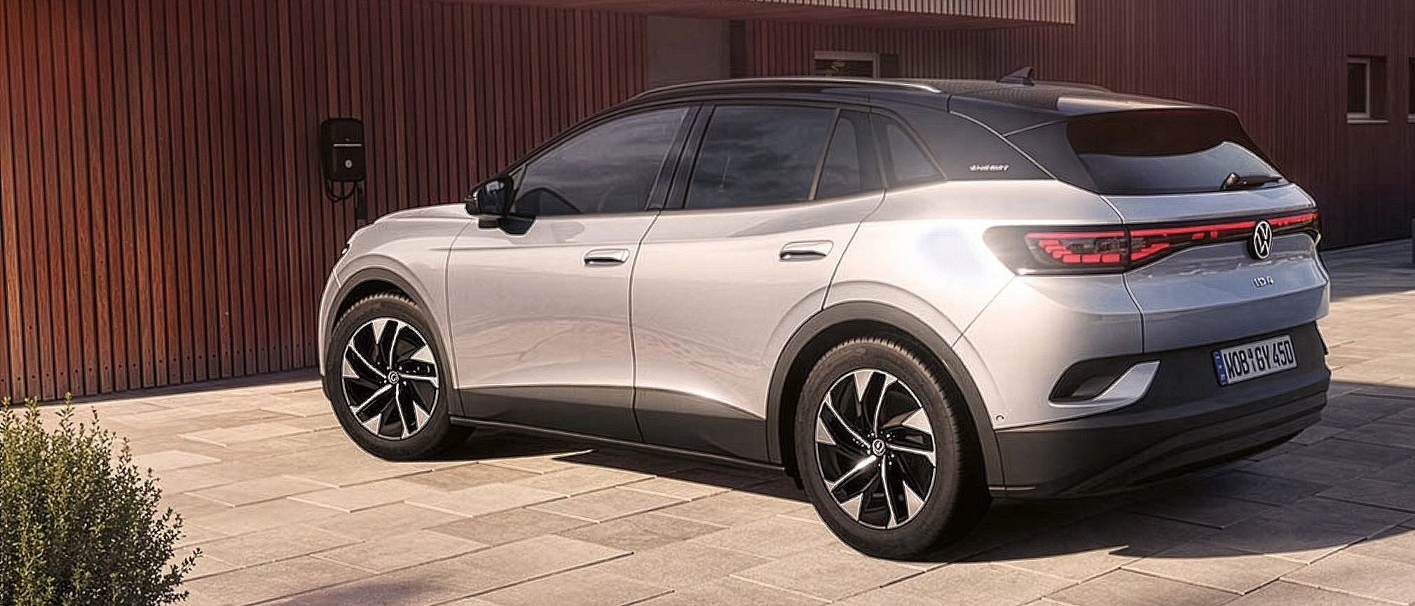 Silberner VW ID.4 Elektro-SUV in schräger Heckansicht vor einem modernen Gebäude mit Holzfassade.