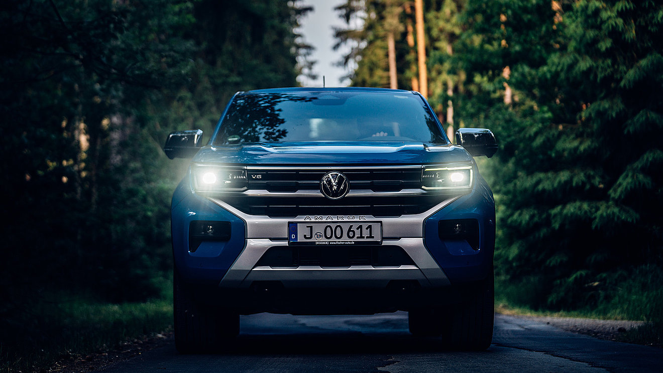 VW Amarok mit eingeschalteten LED-Scheinwerfern in Frontansicht auf einer Waldstraße.