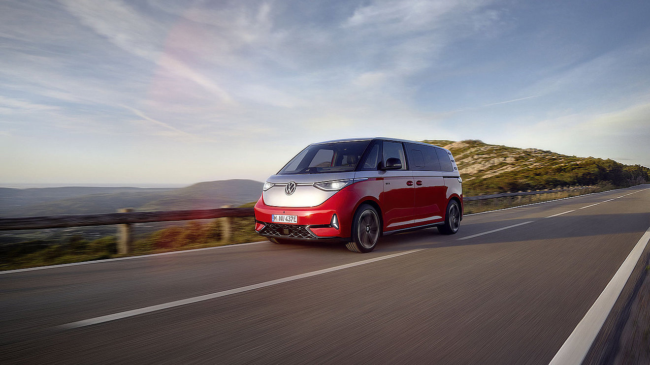 Roter VW ID. Buzz GTX Elektrobus von Volkswagen in moderner Architekturkulisse, Front- und Seitenansicht – erhältlich bei Autohaus Fischer.