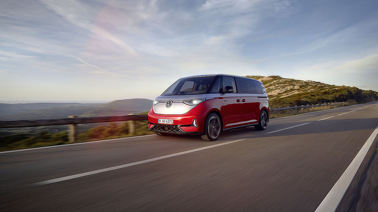Roter VW ID. Buzz GTX Elektrobus von Volkswagen in moderner Architekturkulisse, Front- und Seitenansicht – erhältlich bei Autohaus Fischer.