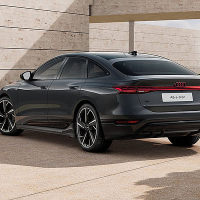 Grauer Audi A6 e-tron in schräger Heckansicht vor moderner Architektur